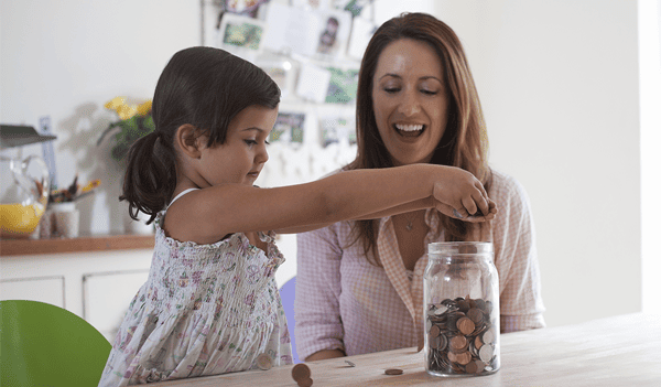 Money and daughter putting coins in a jar