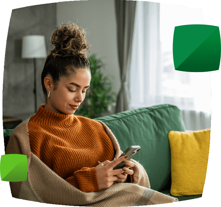 Woman on sofa wrapped in blanket using phone